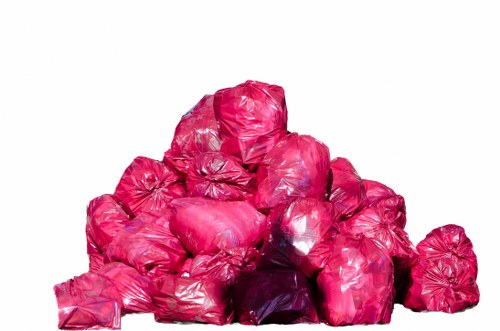 A large pile of pink plastic garbage bags, filled and tightly tied at the top, stacked on top of each other on a plain white background. The bags appear to contain household or office waste and are piled in a somewhat irregular, disorganized manner, suggesting a collection of rubbish awaiting removal. The vibrant pink colour of the bags contrasts with the neutral background, and the plastic material shows some creases and reflections, indicating they are made of standard rubbish bag plastic. The setting is isolated, with no surrounding environment or additional objects visible, focusing solely on the collection of waste bags. This image may relate to rubbish disposal or waste management services provided by companies like Office Clearance Swiss Cottage, serving areas within the NW3 postcode or the Swiss Cottage locale.